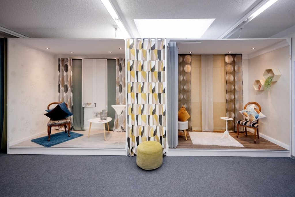Moderne Gardinen-Ausstellung und Wohnraum-Inspiration bei Raumausstattung Storck: Verschiedene Vorhang-Designs, Dekostoffe und Polstermöbel in wohnlichen Kojen präsentiert für individuelle Inneneinrichtung.
